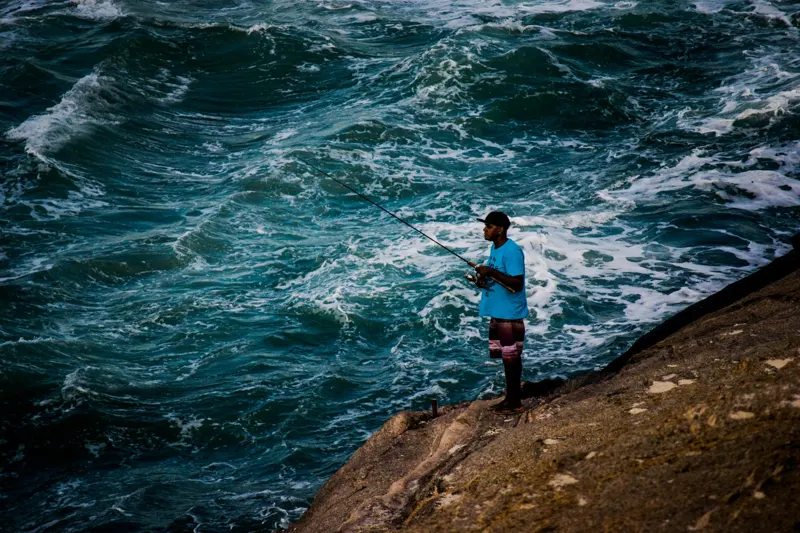 Pescador na pedra do Arpoador com o mar batendo